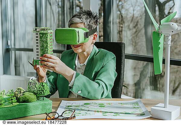 Businesswoman wearing virtual reality simulator holding biophilic architectural model in office