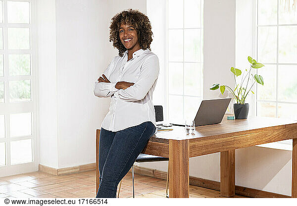 Businesswoman with arms crossed smiling while leaning on table at home