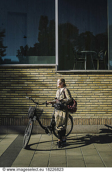 Businesswoman with bicycle standing in front of wall