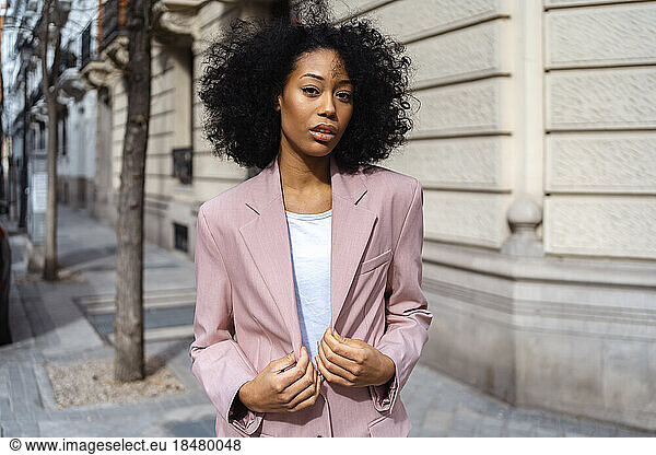 Businesswoman with curly hair wearing blazer at footpath