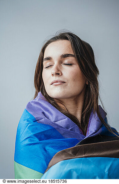 Businesswoman with eyes closed wrapped in rainbow flag