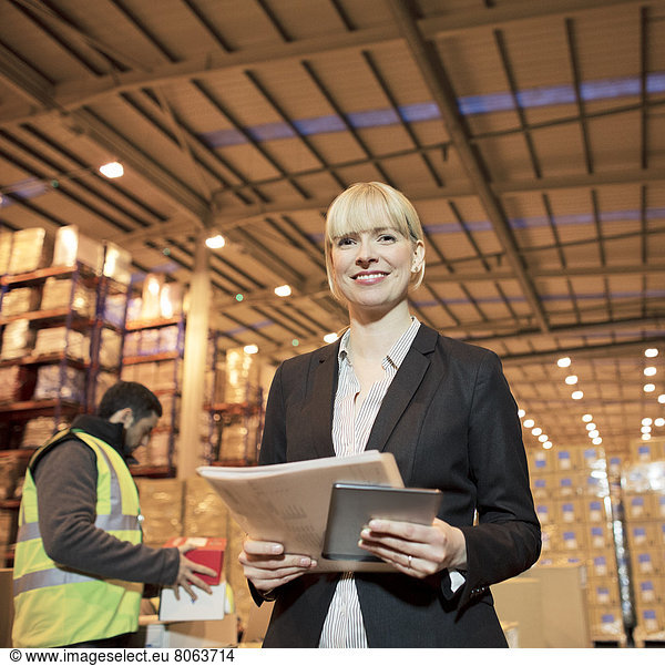 Businesswoman with folder and tablet computer in warehouse