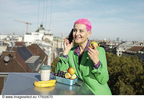 Businesswoman with fruits talking on mobile phone at rooftop