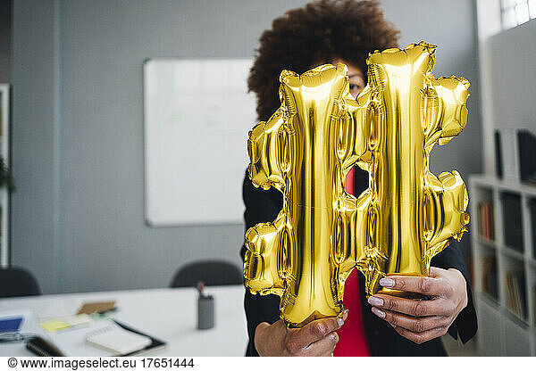 Businesswoman with golden hashtag symbol balloon in front of face