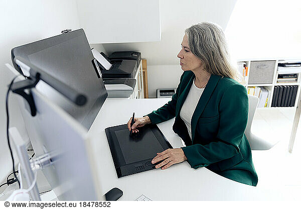 Businesswoman with graphic tablet sitting at desk in office