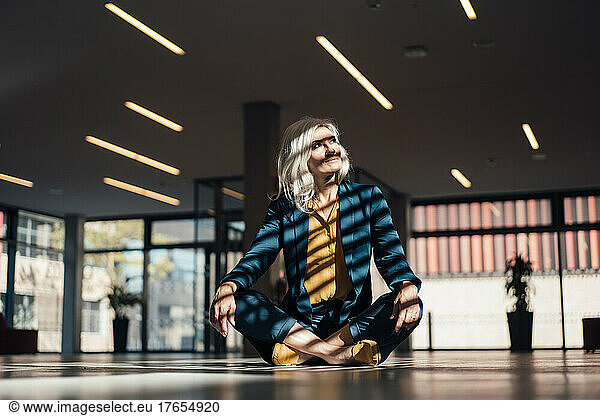 Businesswoman with gray hair sitting cross-legged in office