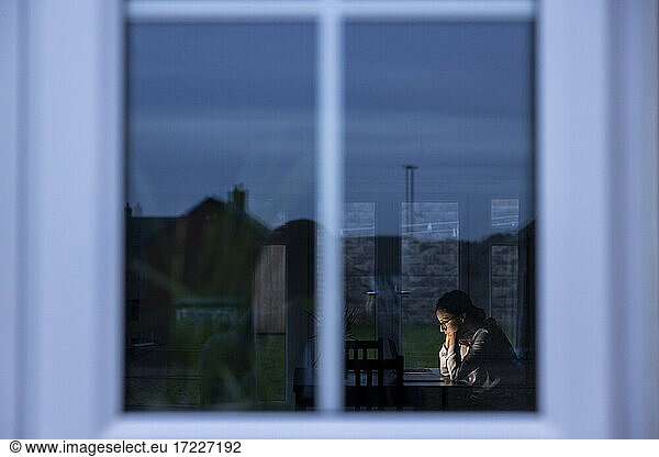 Businesswoman with hand on chin looking at laptop seen through window