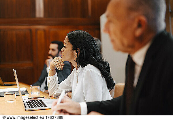 Businesswoman with hand on chin sitting amidst male colleagues in board room meeting