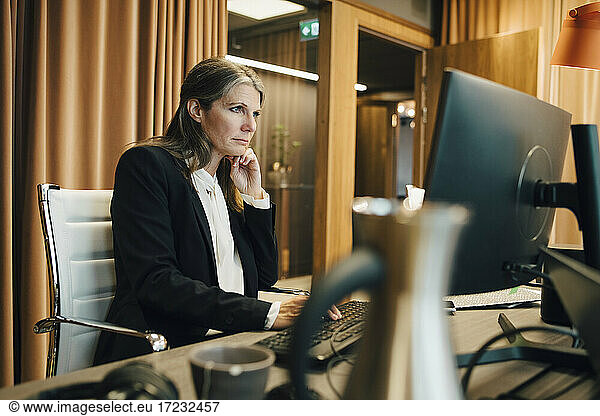 Businesswoman with hand on chin working over computer in office