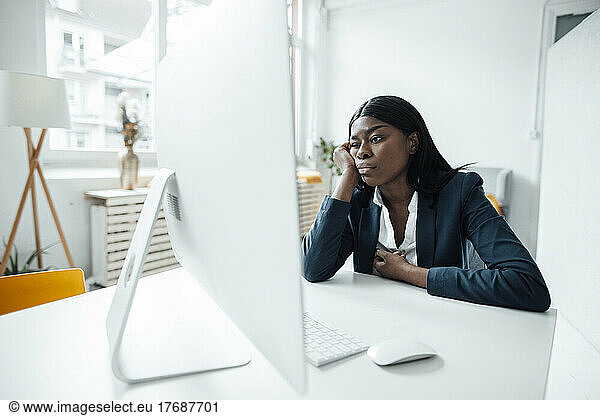 Businesswoman with head in hand looking at desktop PC