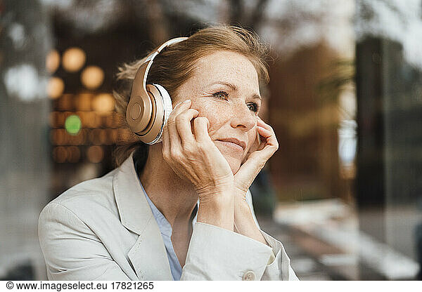 Businesswoman with head in hands listening music through wireless headphones at cafe