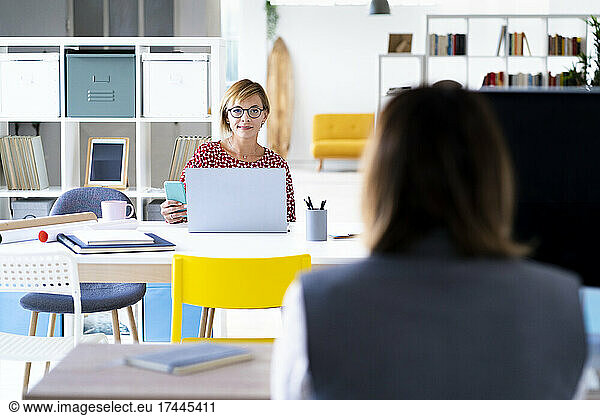 Businesswoman with laptop looking at female colleague in office