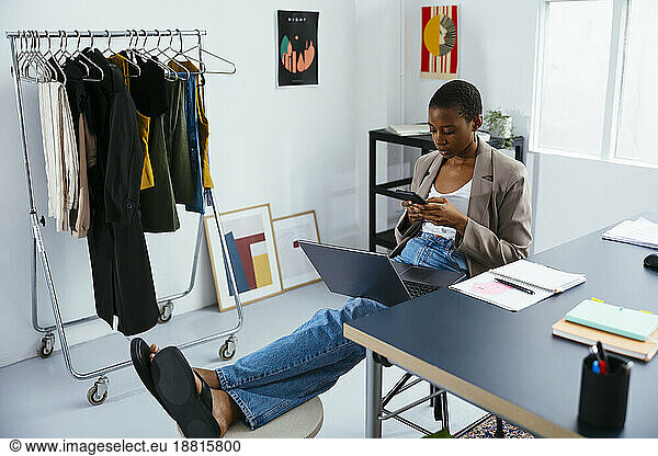 Businesswoman with laptop using smart phone sitting at office