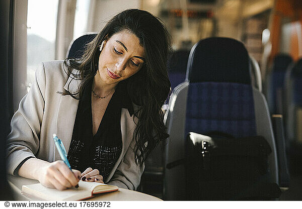 Businesswoman with long hair writing on diary while sitting in train