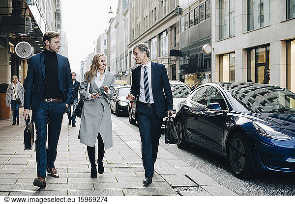 Businesswoman with male colleagues walking on sidewalk in city