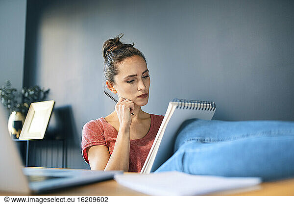 Businesswoman with note pad and pencil relaxing at desk in home office