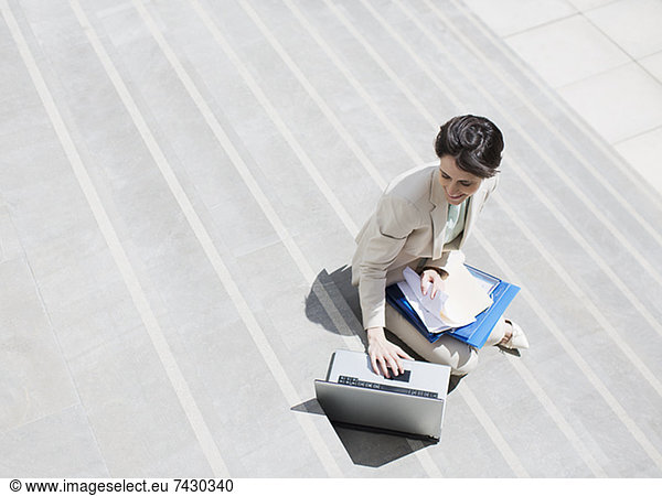 Businesswoman with paperwork using laptop on urban steps
