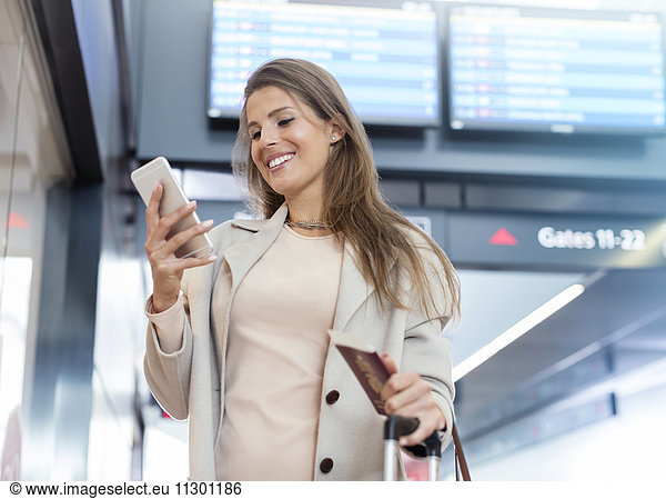 Businesswoman with passport using cell phone in airport