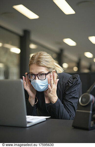 Businesswoman with protective face mask working on laptop at office desk
