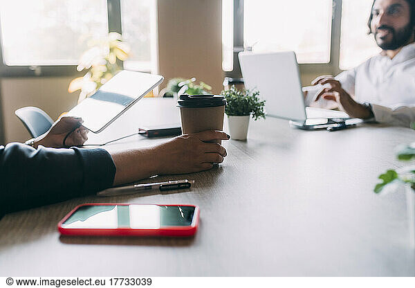 Businesswoman with reusable coffee cup by colleague in office