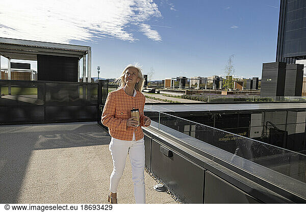 Businesswoman with reusable coffee cup walking on footbridge
