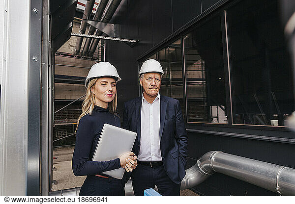 Businesswoman with senior colleague standing near pipe at factory