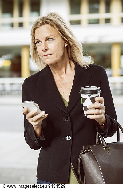 Businesswoman with smart phone and disposable coffee cup looking away outdoors