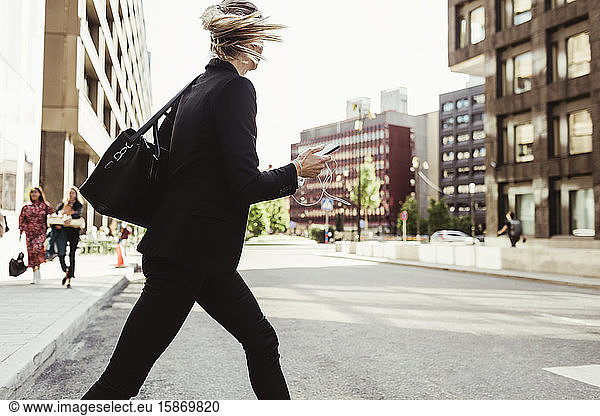 Businesswoman with smart phone crossing street