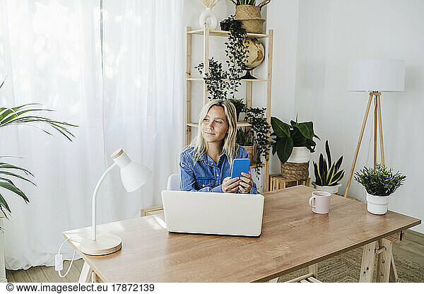 Businesswoman with smart phone sitting at desk in home office