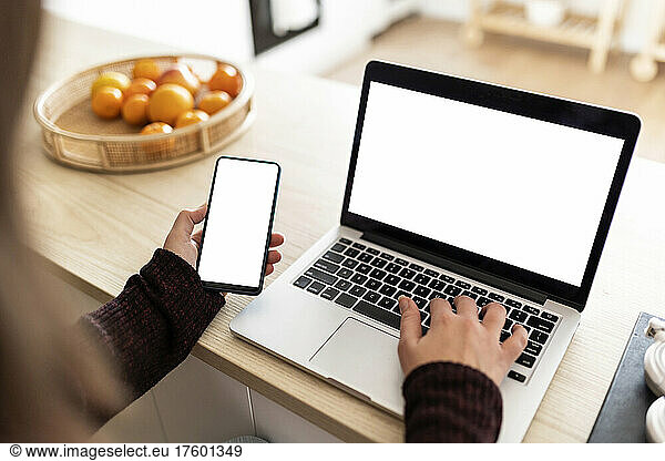 Businesswoman with smart phone using laptop at home