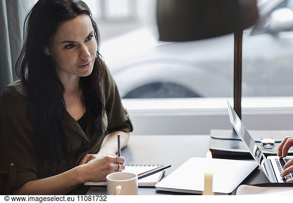 Businesswoman with spiral notebook while sitting at table in modern office