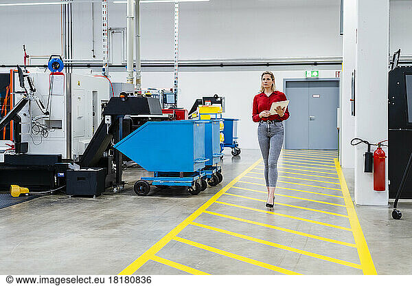 Businesswoman with tablet PC walking on markings in factory