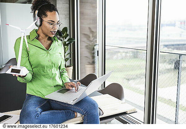 Businesswoman with wind turbine model working on laptop at office