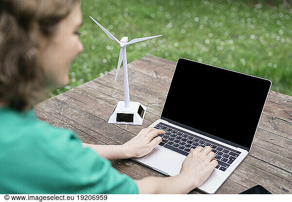 Businesswoman working on laptop by wind turbine model on table