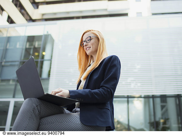 Businesswoman working on laptop outside office building