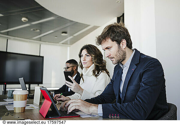 Businesswoman working on laptop sitting by colleagues at desk in office