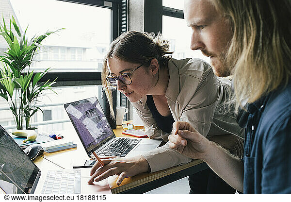 Businesswoman working on laptop with male colleague in startup company