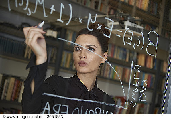 Businesswoman writing formula on glass wall