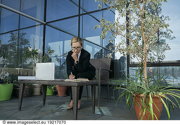 Businesswoman writing in diary on terrace of business center