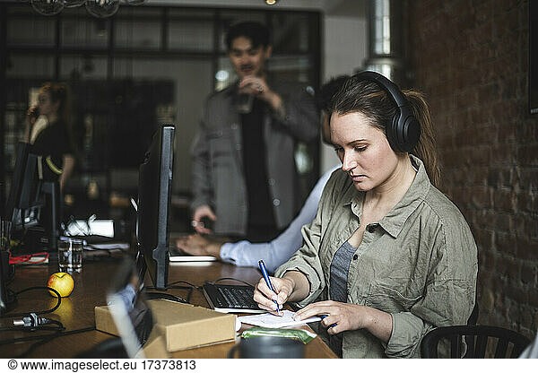 Businesswoman writing in note pad while working in office