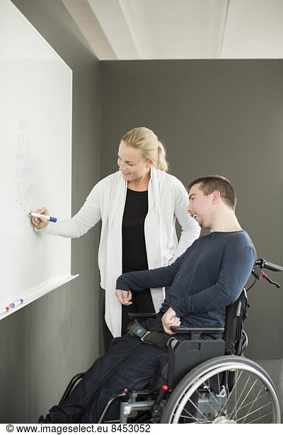 Businesswoman writing on whiteboard while working with disabled businessman in office