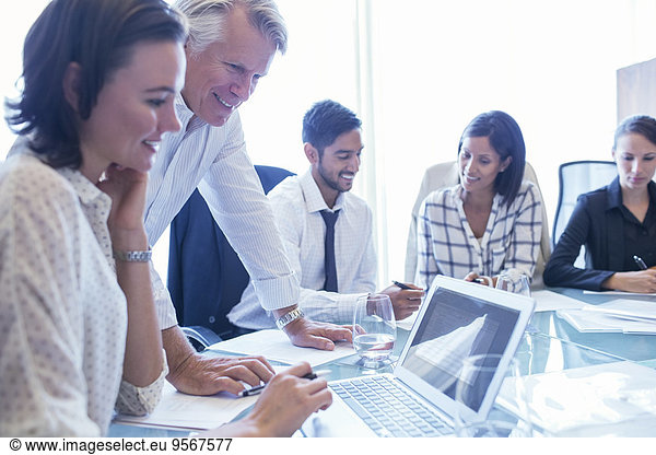 Businesswomen and businessmen sitting at conference table  using laptop and smiling