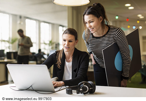 Businesswomen discussing over laptop in creative office