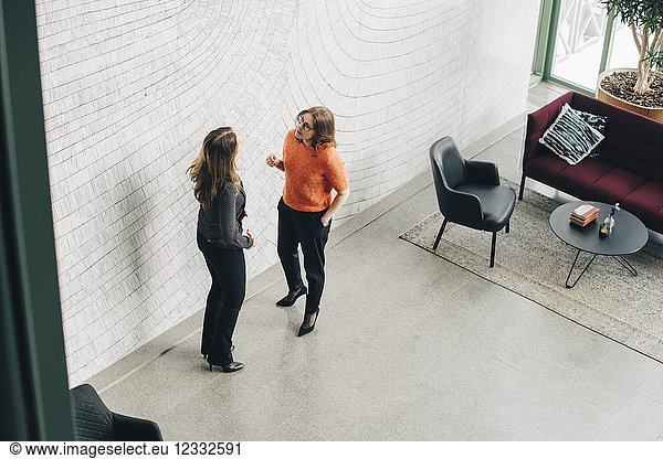 Businesswomen discussing while standing by wall at office