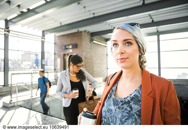 Businesswomen holding coffee cup while standing at railroad station