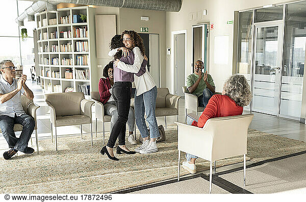 Businesswomen hugging each other by colleagues sitting in office