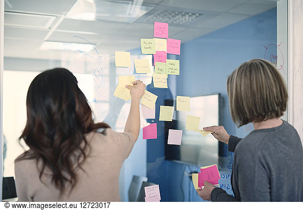 Businesswomen sticking adhesive notes on glass in office