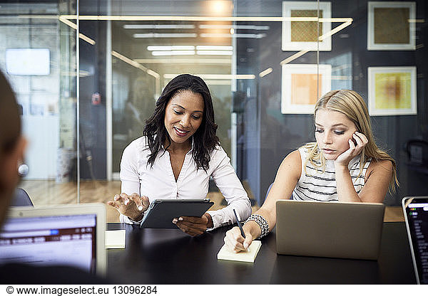 Businesswomen using technologies while sitting in meeting at conference table