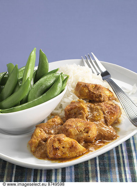 Butter Chicken and rice on plate with bowl of snap peas  studio shot