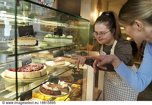 Cafe owner with down syndrome advising customer to choose cake in coffee shop
